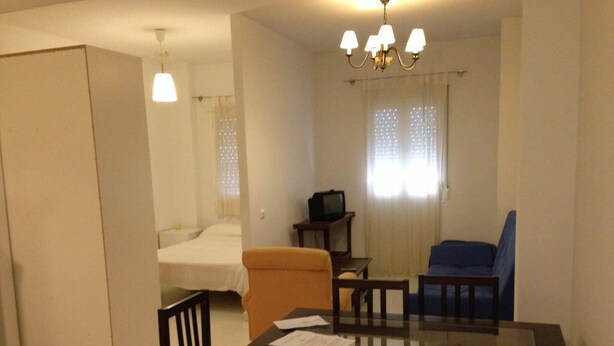 Habitación de hotel pequeña con cama, una mesita con sillas, televisión y ventana con cortinas.