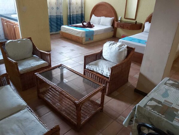 Habitación con cama, dos sillas de mimbre, una mesa con superficie de vidrio y una mesita con mantel estampado.