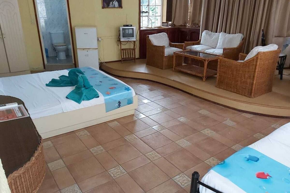 Een hotelkamer met twee bedden, een zithoek met rieten meubels, een televisie en een raam met gordijnen.