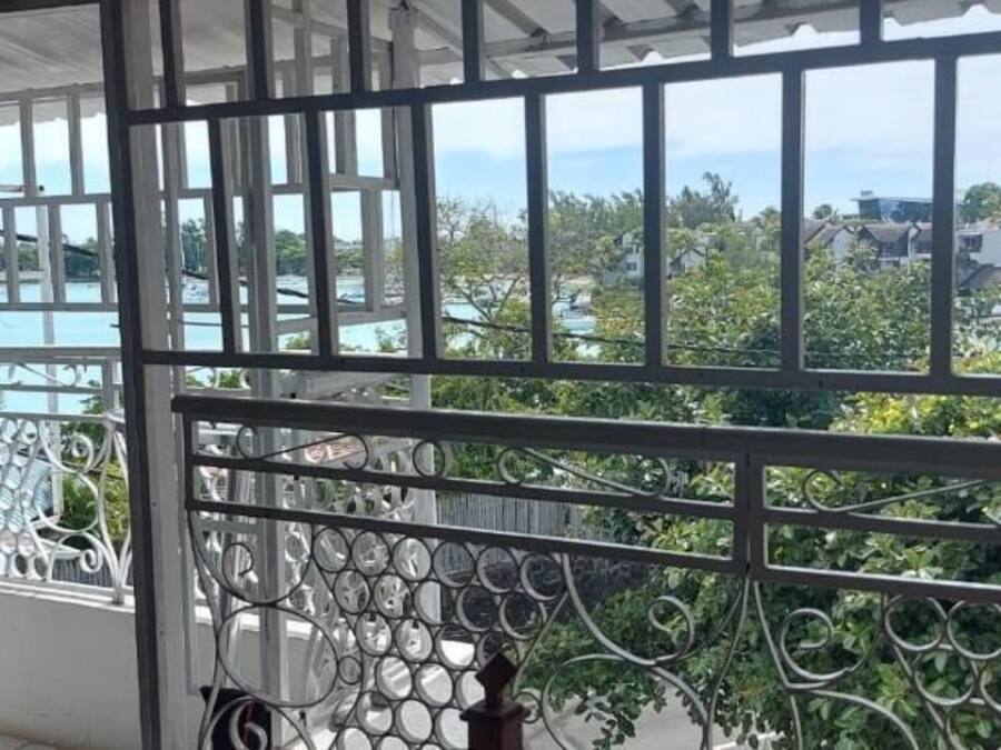Un balcón con barandilla de metal y vista a una zona residencial con casas y vegetación.