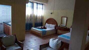 Habitación de hotel con dos camas, una mesita, una silla, ventana con cortinas y baño con lavamanos y espejo.
