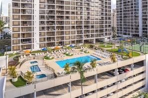 A multi-story hotel with a rooftop swimming pool, sun loungers, and a parking garage.
