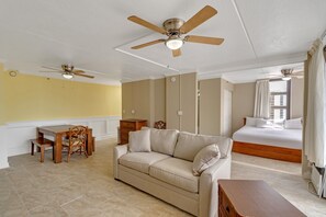 Una habitación de hotel con una cama, un sofá, una mesa de comedor con sillas y dos ventiladores de techo.