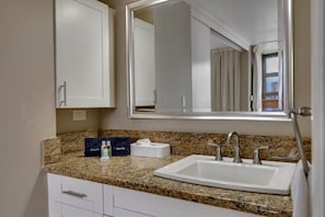 Un baño con encimera de granito, un lavabo blanco, un espejo y un perchero para toallas.