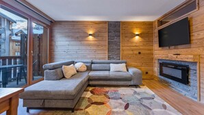 Una sala de estar acogedora con un sofá modular, una chimenea y un televisor en la pared.