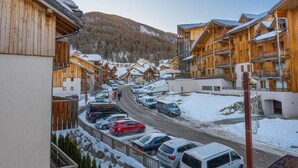 Una hilera de cabañas de madera con balcones, un estacionamiento y una montaña nevada al fondo.