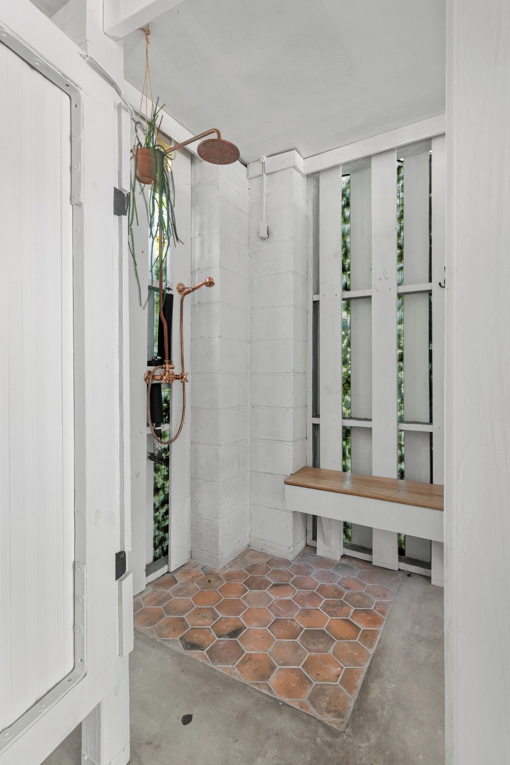 A shower with a wooden bench, a hanging plant, and a tiled floor.