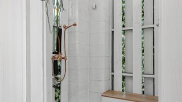 A shower with a wooden bench, a hanging plant, and a tiled floor.