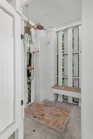 A shower with a wooden bench, a hanging plant, and a tiled floor.