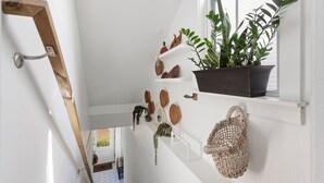 Una escalera con paredes blancas, estantes con plantas y un ventanal con planta en maceta.