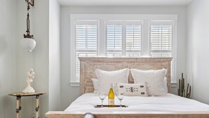 Un dormitorio con una cama grande, una mesita de noche con una escultura, una botella de vino y dos copas.
