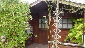 Una cabaña de madera con un porche de madera, una estructura de celosía y una puerta de madera con ventanas.