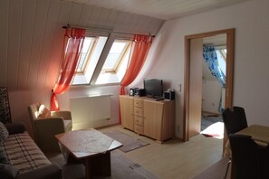 A compact living space with a sofa, a small table, a cabinet with a television, and a window with curtains. - Holiday Wittow (Wiek)