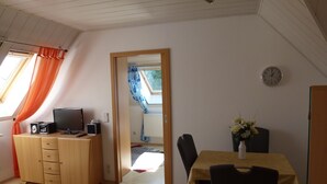 Una habitación con un escritorio de madera, una silla, un televisor en un mueble y un reloj en la pared.