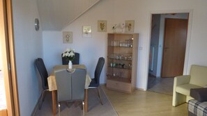 A dining area with a table and chairs, a cabinet with glassware, and a door leading to another room. - Holiday Wittow (Wiek)