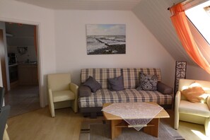 A living room with a sofa, a coffee table, and a painting of a beach scene. - Holiday Wittow (Wiek)