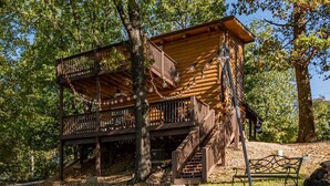 A wooden cabin with a balcony and stairs, surrounded by trees.