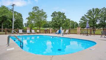 A swimming pool with a diving board, lounge chairs, and a stone pillar.