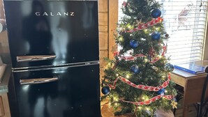 A kitchen with a black refrigerator, a Christmas tree, and a window with blinds.