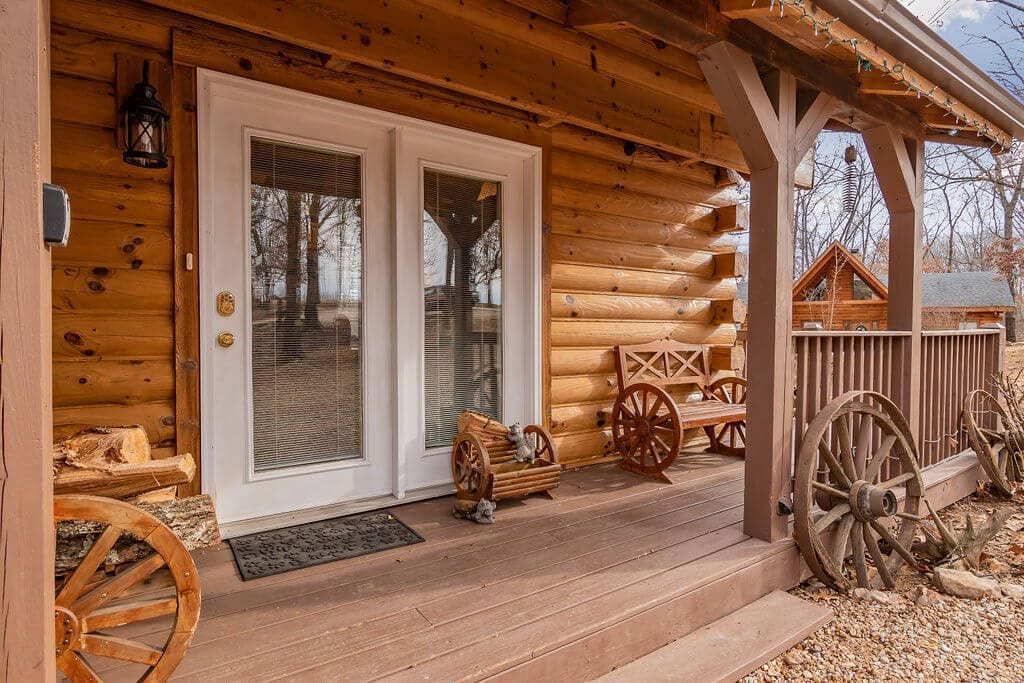 Une cabane en rondins avec une véranda en bois, une porte à deux battants et un petit espace de véranda agrémenté de roues en bois et d’un banc.