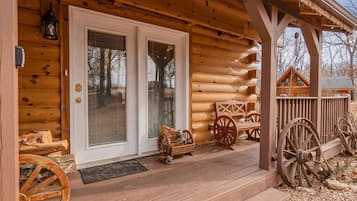 Une cabane en rondins avec une véranda en bois, une porte à deux battants et un petit espace de véranda agrémenté de roues en bois et d’un banc.