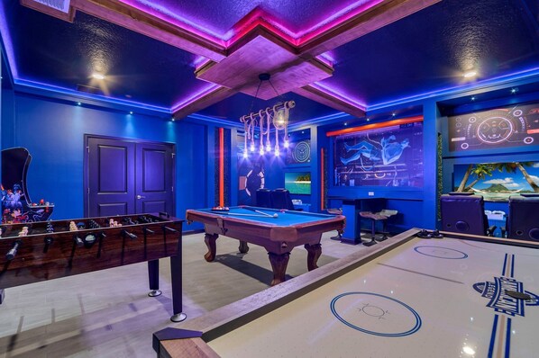 A room with a pool table, foosball table, and a projection screen displaying a game.