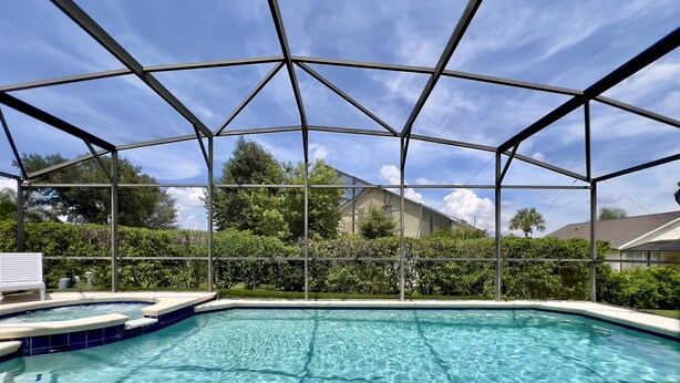 Une piscine aux eaux cristallines, dotée d’un espace abrité, entourée de verdure et avec une maison en arrière-plan.