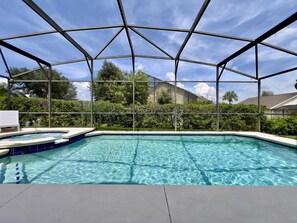 A clear swimming pool with a covered area, surrounded by greenery and a house in the background.