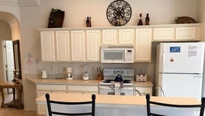 Une cuisine avec des meubles blancs, un four à micro-ondes, une cuisinière, un réfrigérateur et deux chaises.