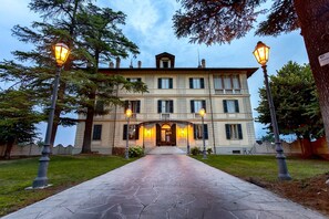 Un edificio grande de varios pisos con una fachada simétrica, una entrada central con porche cubierto y un camino pavimentado que conduce a la entrada.