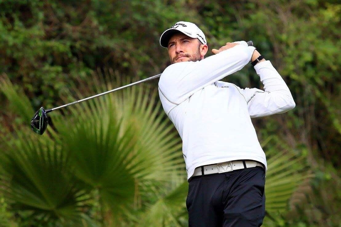 Ein Golfspieler im Schwung auf einem Golfplatz, im Hintergrund üppiges Grün.