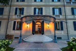 Une entrée imposante, avec un escalier couvert menant à une porte, de part et d’autre de laquelle se trouvent deux appliques murales illuminées.