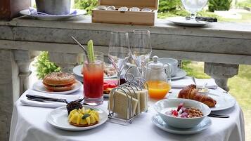 A table set with breakfast items including a croissant, a sandwich, a fruit bowl, a glass of juice, and a drink with a straw.
