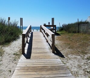 A wooden boardwalk leading to a beach with a clear view of the ocean.
