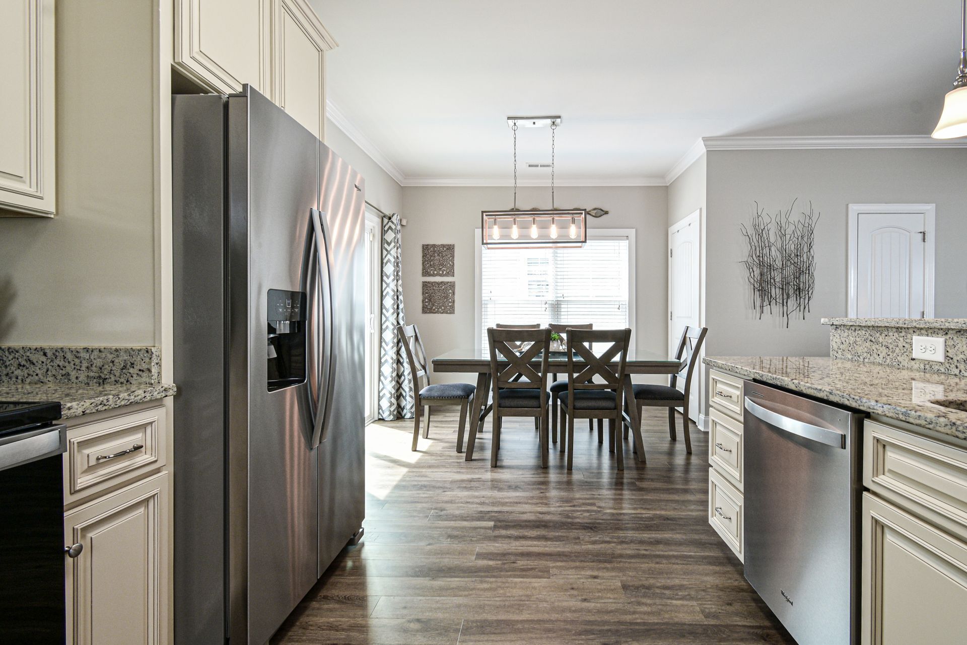 A modern kitchen with a stainless steel refrigerator, granite countertops, and a dining area with a wooden table and chairs.
