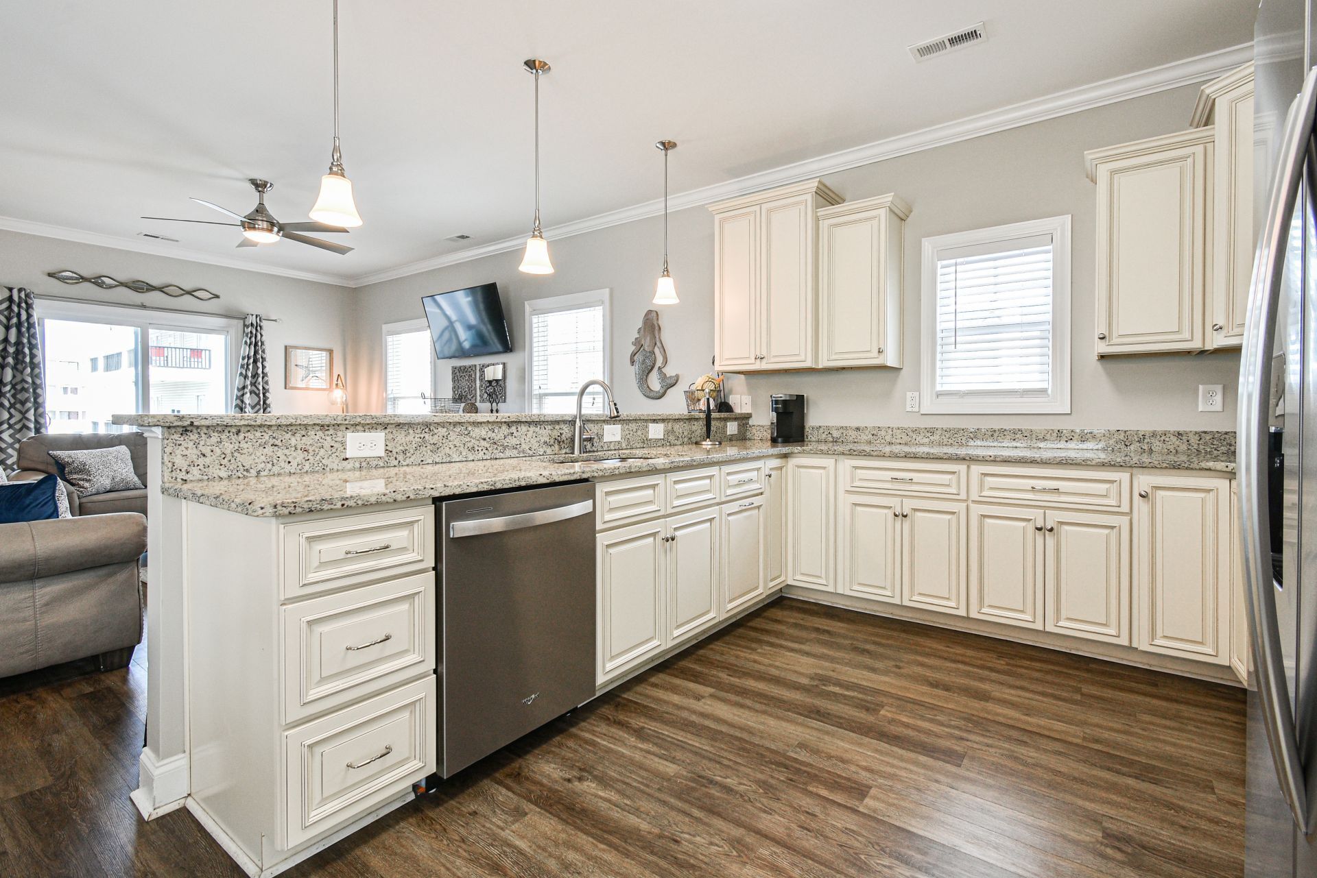 A modern kitchen with white cabinetry, granite countertops, a dishwasher, and a built-in oven.