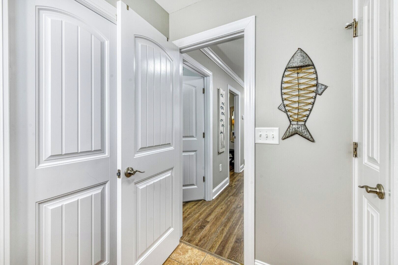 A hallway with white doors and a decorative fish wall art piece.