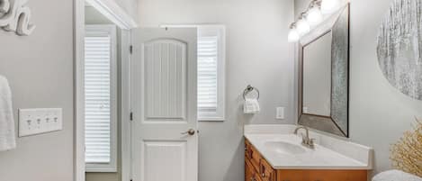 A bathroom with a white door, a vanity with a mirror, and a towel rack.