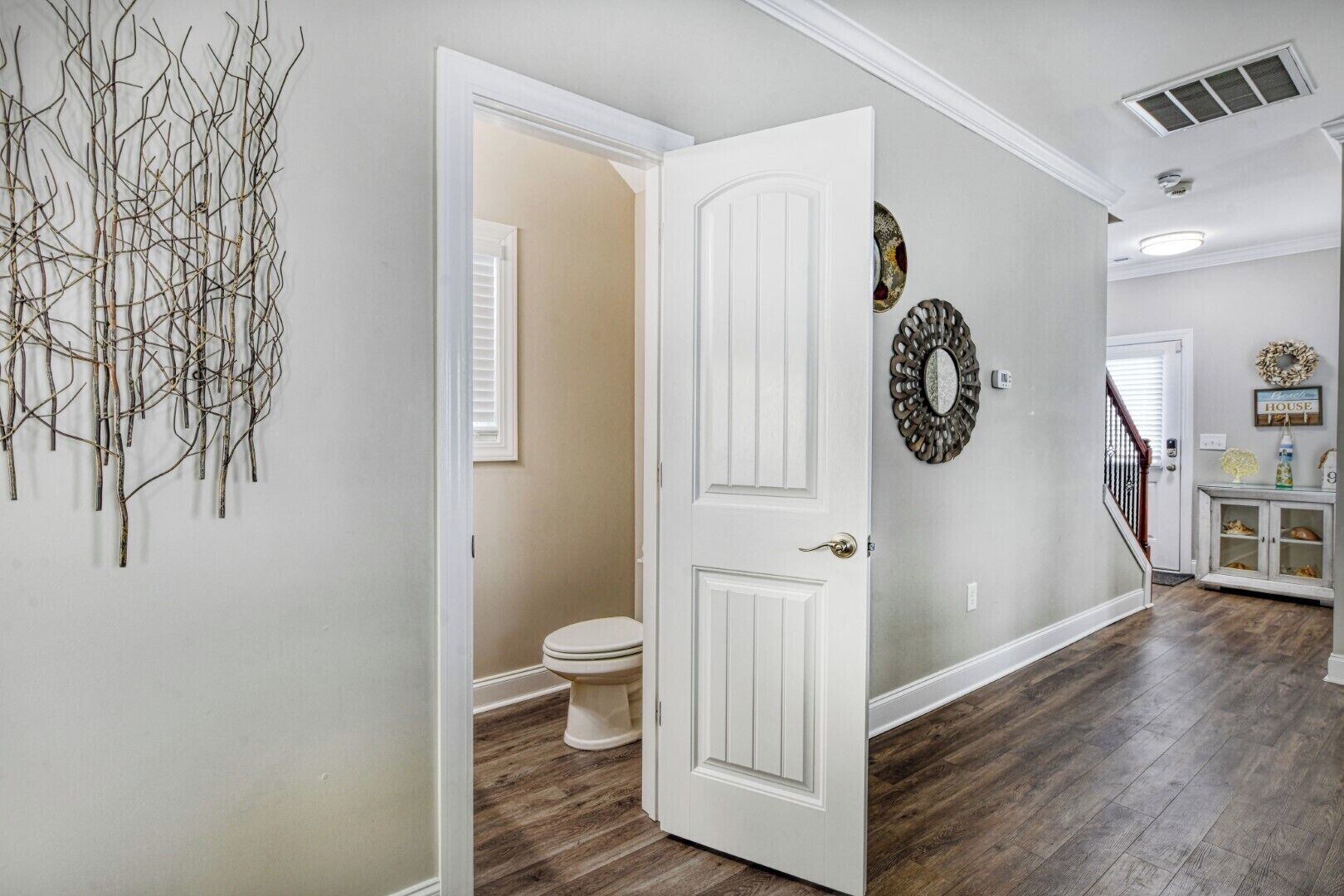A hallway with a white door leading to a bathroom, a decorative wall piece, and a staircase.