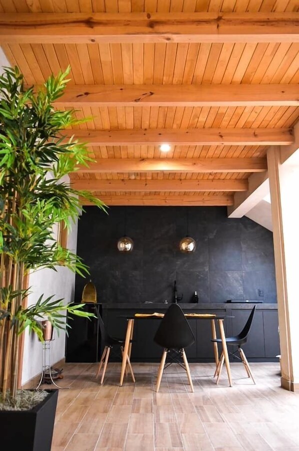 Een moderne keuken met een zwarte achterwand, houten balken in het plafond en een eethoek met zwarte stoelen.