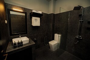 A modern bathroom with a dark tiled wall, a white sink, a glass-enclosed shower, and a toilet. - Scenic Bay Weligama (Weligama)