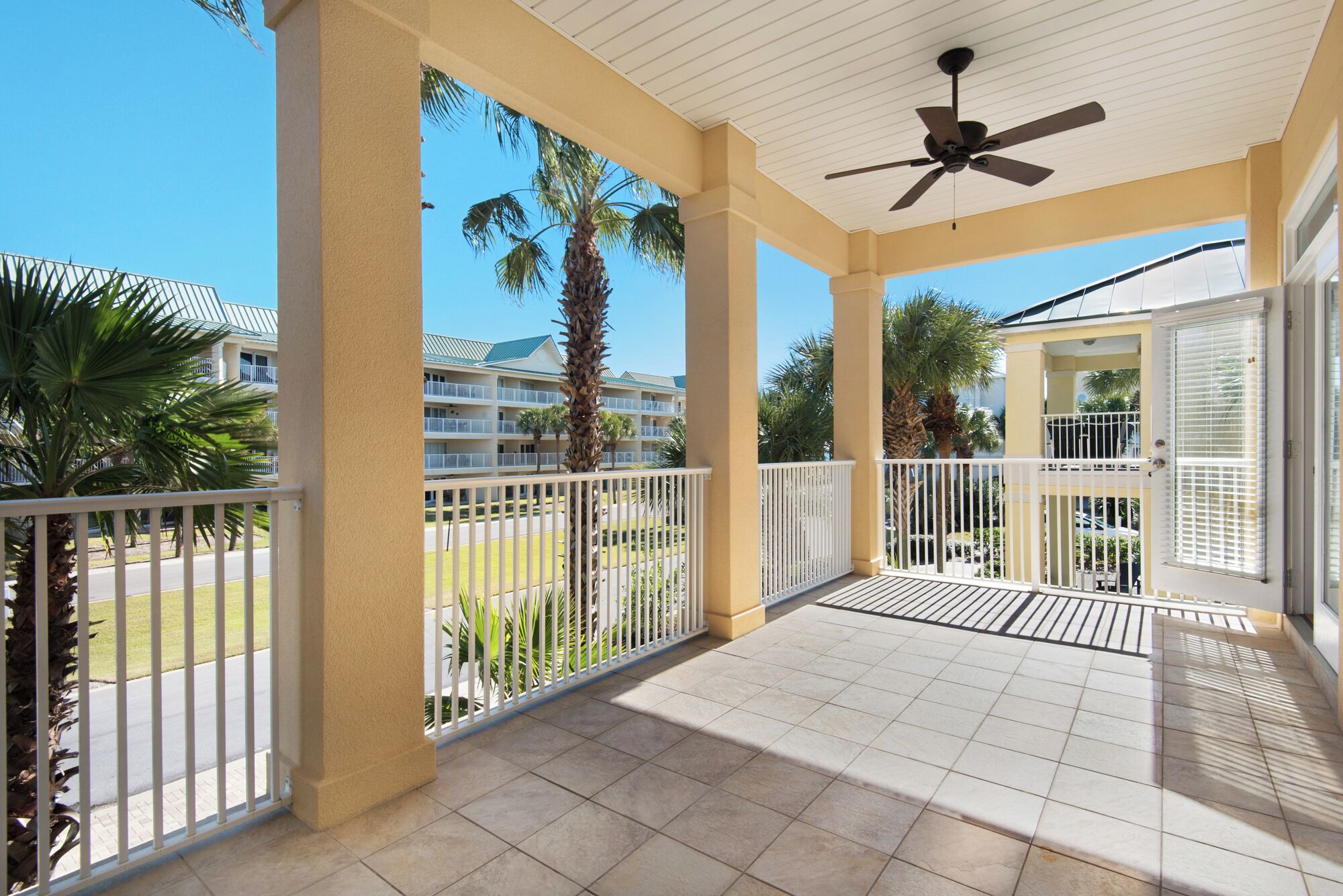 A covered outdoor area with a ceiling fan, white railings, and a view of a hotel building.