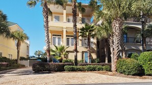 Un hotel de varios pisos con balcones, palmeras y un camino de entrada pavimentado.