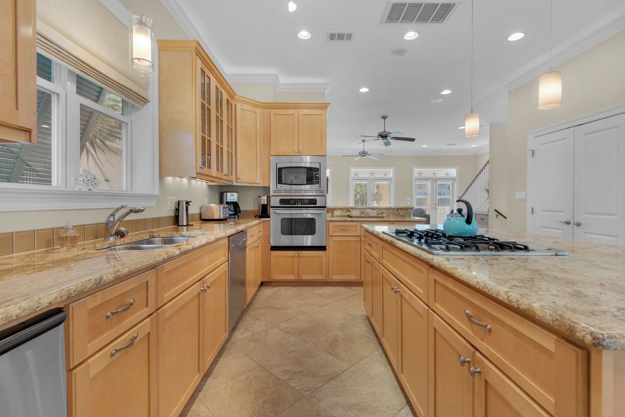 A kitchen with wooden cabinets, granite countertops, stainless steel appliances, and a ceiling fan.