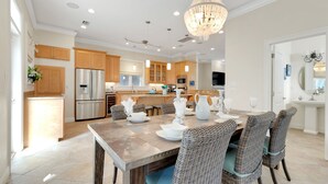 Una cocina moderna con armarios de madera, electrodomésticos de acero inoxidable y un comedor con sillas de mimbre y una araña.