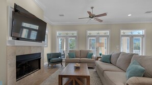 Una sala de estar con chimenea, televisor, ventilador de techo y un ventanal decorado con estrellas.
