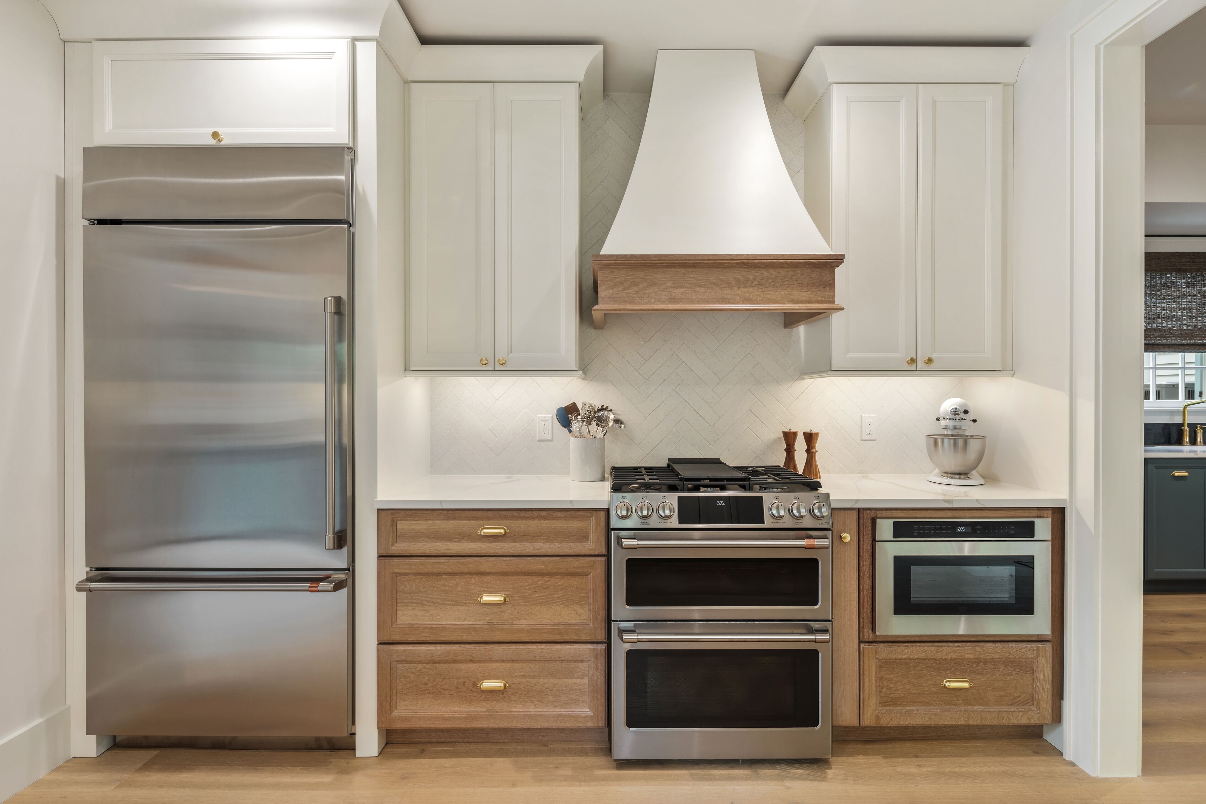 Une cuisine moderne dotée d’appareils électroménagers en acier inoxydable, de meubles de rangement en bois et d’un dosseret de carrelage disposé en motif chevron.
