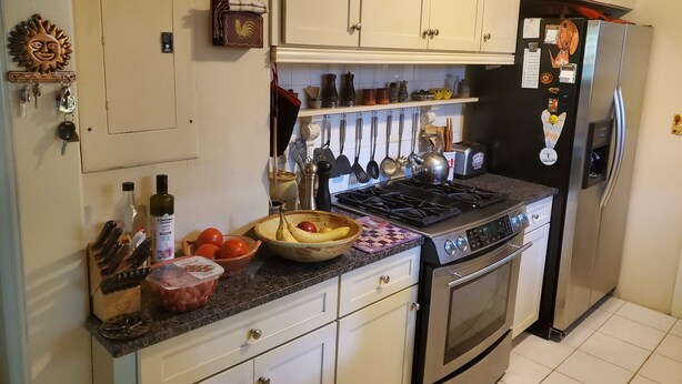 A kitchen with white cabinets, a stove, an oven, and a refrigerator. There are various kitchen utensils and a bowl of fruit on the counter. - Downtown Historic district at Cascades Park, Best location (Tallahassee)