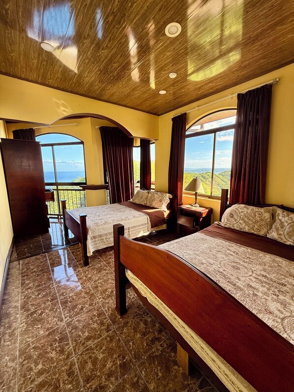 A hotel room with two beds, a balcony, and large windows offering a view of the landscape. - Prime location- Two Bay spectacular view + infinity pool + 30min to LIR airport (Playa Hermosa)