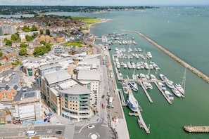 An aerial view of a coastal town with a marina, buildings, and a road.